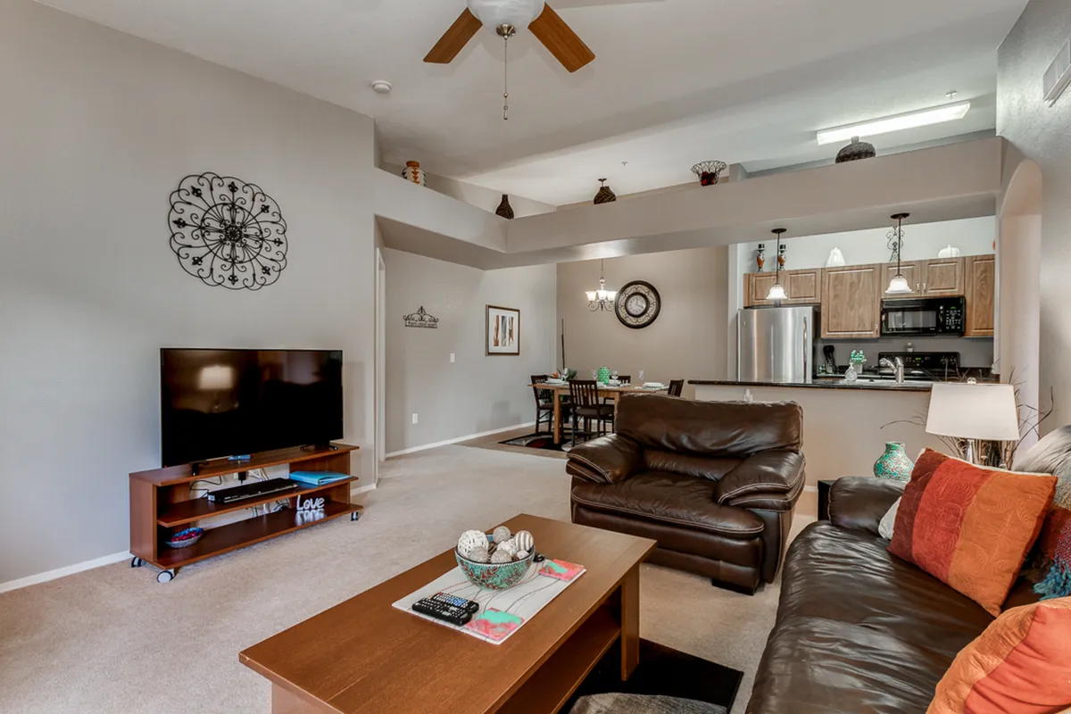 A warm and welcoming living/dining space with a comfortable brown leather sofa facing a coffee table and a TV on a stand. The adjacent dining area with a wooden table is partially visible, echoing the open-concept design and the multifunctional aspect of the space.