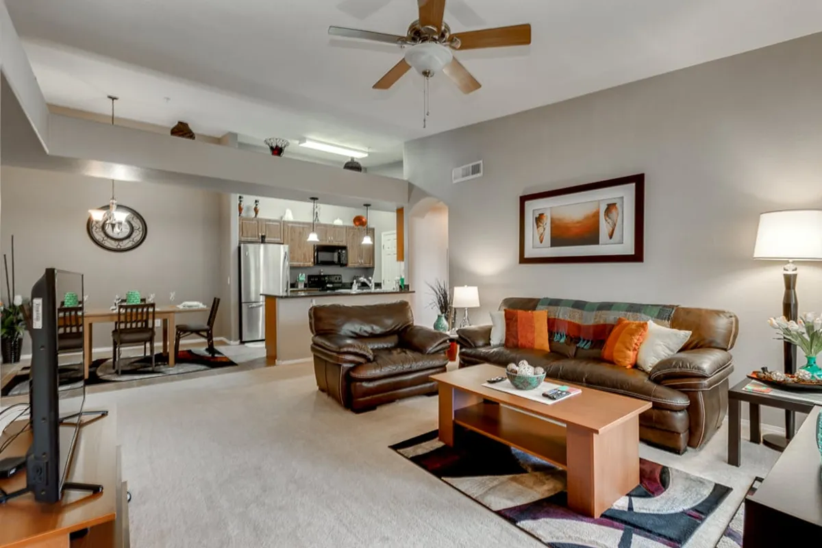 A stylish interior scene showing a leather sofa, dining area, kitchen, and wall art. The room is bright and airy, with modern décor and comfortable seating arranged for both lounging and entertaining guests.