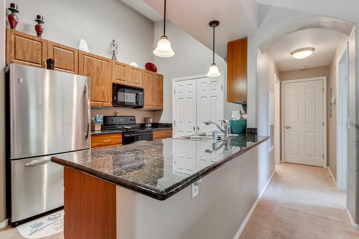 A stylish kitchen featuring granite countertops, stainless steel appliances (including a modern stove and microwave), warm wood cabinetry, and pendant lighting. The inviting atmosphere suggests a space designed for both cooking and casual entertaining.