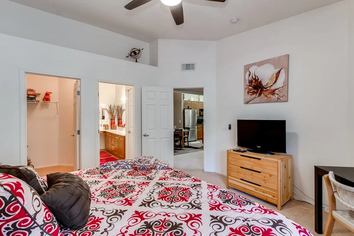 A comfortable bedroom featuring a neatly made bed with decorative bedding, a television mounted across from the bed, and tasteful artwork on the wall. The space exudes a cozy and welcoming atmosphere, ideal for relaxation and unwinding.