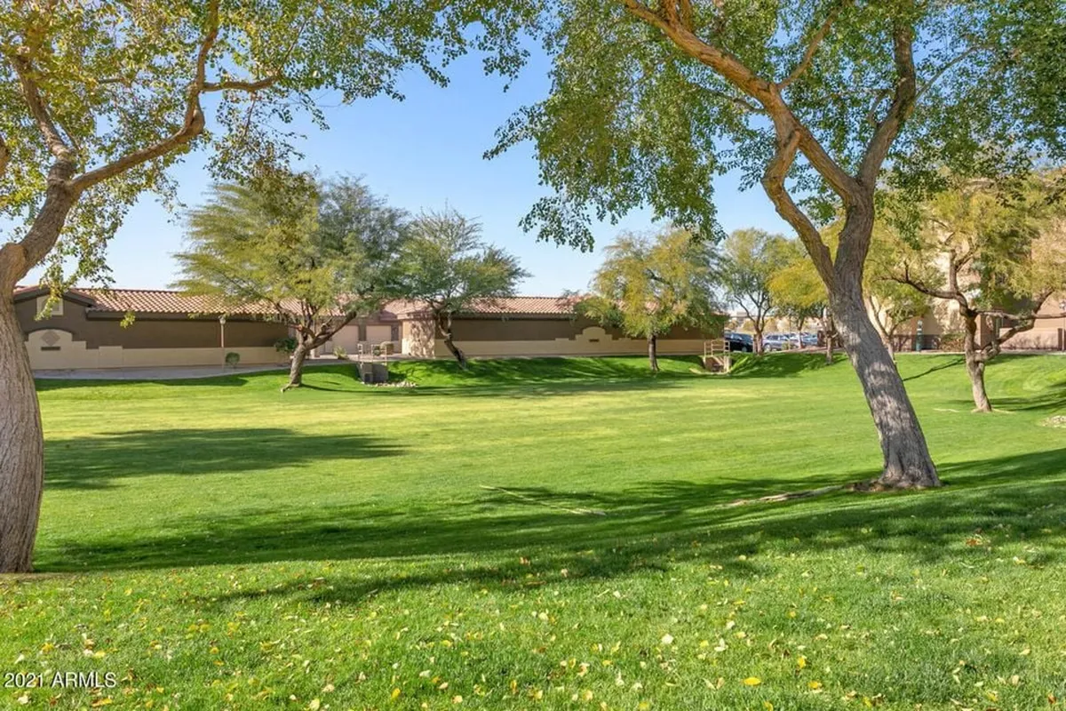A wide exterior shot showing a lush green lawn, mature trees, and a well-maintained pathway. The serene setting invites residents to relax outdoors, enjoy nature, or take a peaceful stroll around the community.