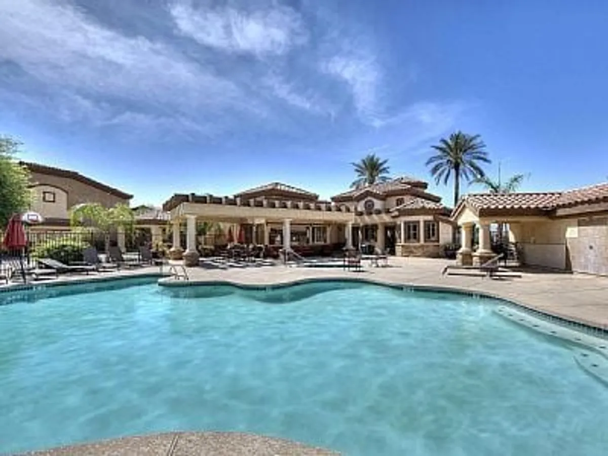 A vibrant community swimming pool area framed by tall palm trees, with inviting lounge chairs and an outdoor dining setup. The pool sparkles under the sun, and the space is ideal for social gatherings or relaxing afternoons.