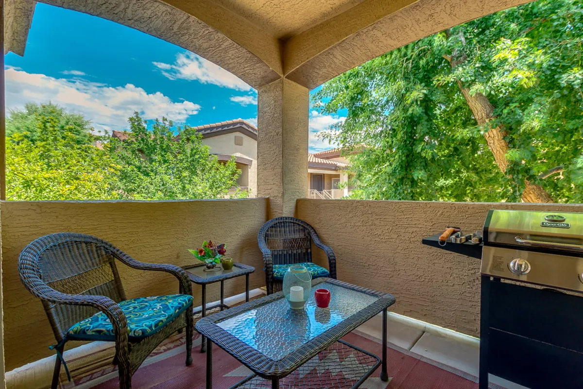 An outdoor seating area with a grill, decorated table, and comfortable chairs. The area suggests a welcoming spot for barbecues, evening gatherings, or casual outdoor meals, surrounded by attractive landscaping.