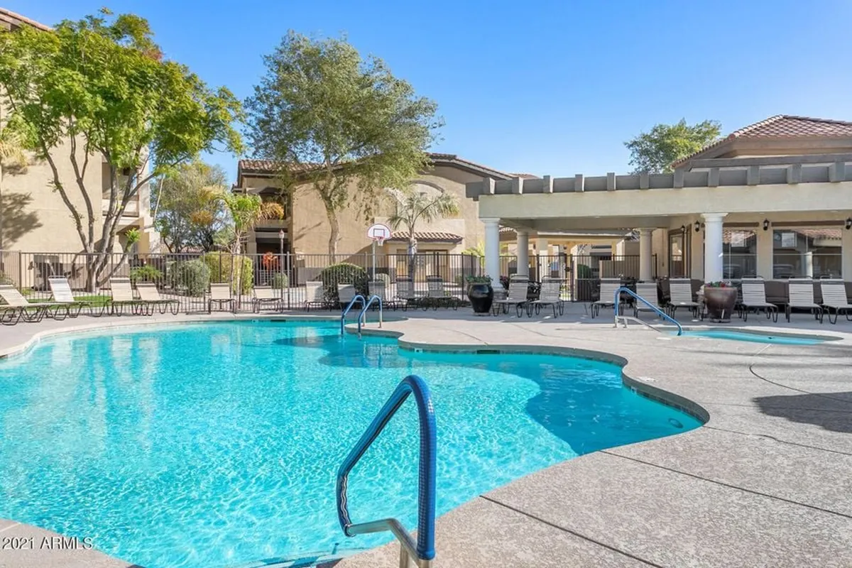 This image showcases a vibrant resort-style swimming pool surrounded by lounge chairs, lush greenery, and a covered patio, inviting residents and guests to relax or socialize after a day of adventure. The water sparkles in the sunlight, and the setting expresses a cheerful, leisure-focused community atmosphere.