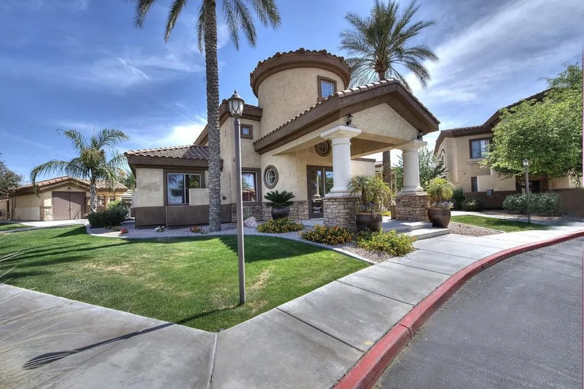 An inviting exterior view featuring elegant entrance columns, tall palm trees, and a beautifully landscaped garden with decorative stonework. This scene conveys a sense of arrival and connection to the outdoors, hinting at tranquil evenings, social gatherings, and the lush environment surrounding the property.