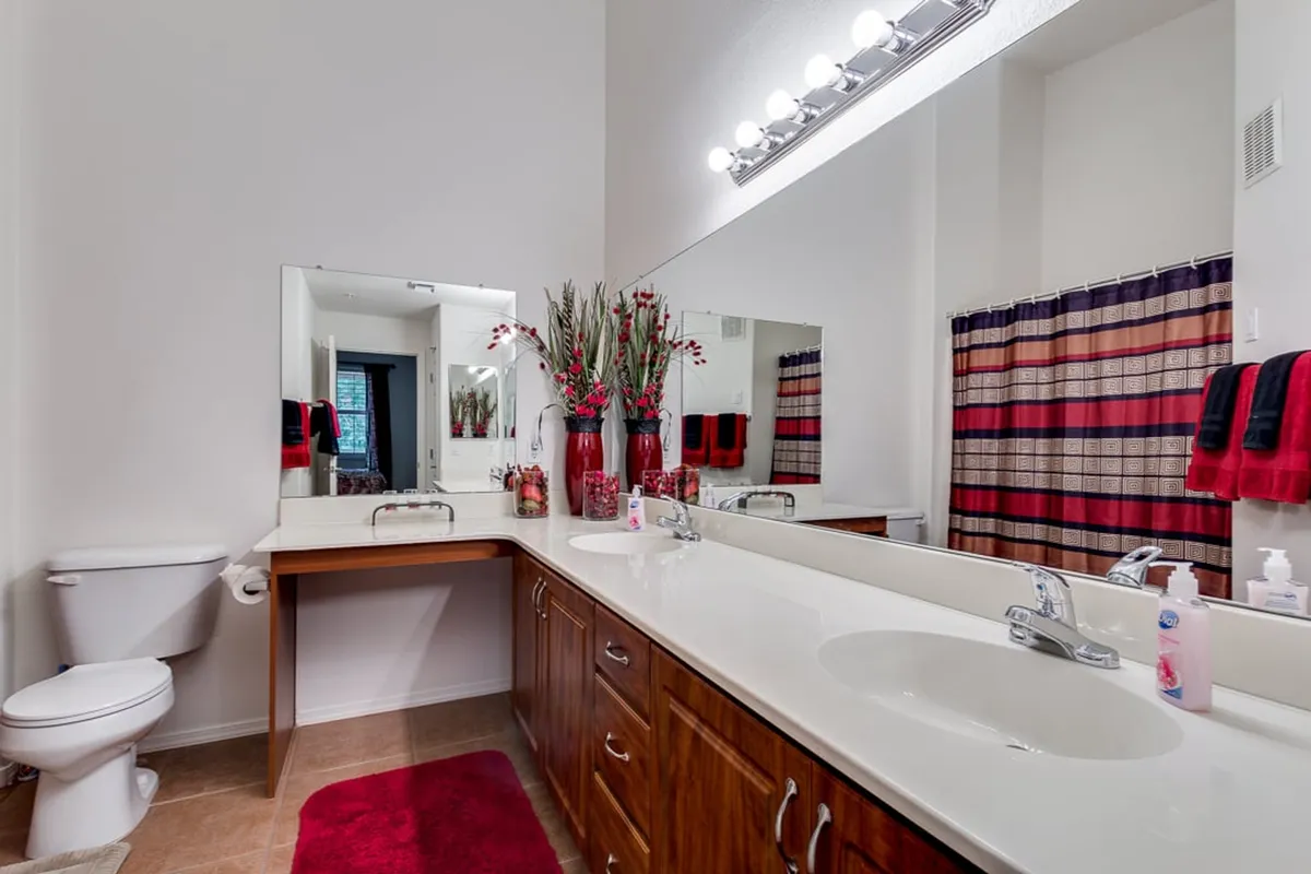 A modern bathroom with double sinks, stylish faucets, a large framed mirror, a decorative vase with fresh flowers, and a colorful shower curtain. The space feels tranquil and spa-like, ideal for personal grooming and relaxation.