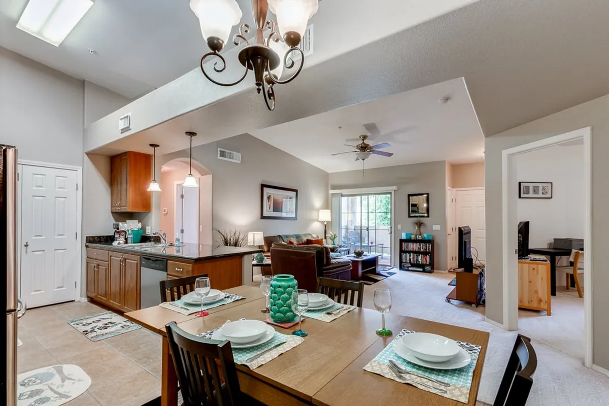 A spacious open-plan interior with a dining table set for a meal, a kitchen island with a bar area, and the living room visible in the background. The layout creates a seamless flow between the kitchen, dining, and living spaces, ideal for gatherings and easy conversation.